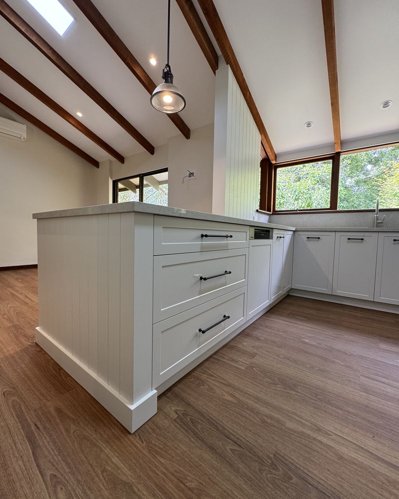 White shaker island and perimeter cabinetry leading to timber-framed windows over the garden