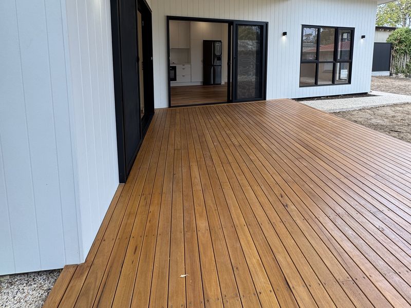 Covered timber deck with a ceiling fan beside white vertical cladding and black-framed sliding doors
