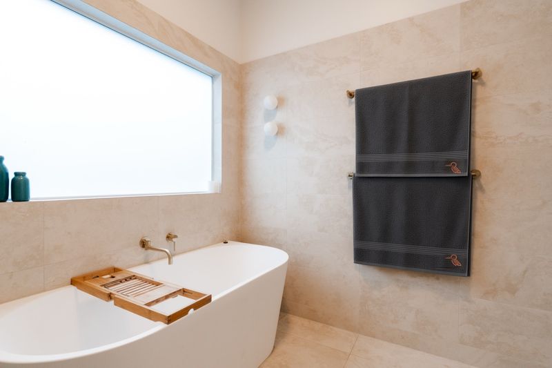 Freestanding bath with stone-look tiles, and charcoal towels on a brass rail