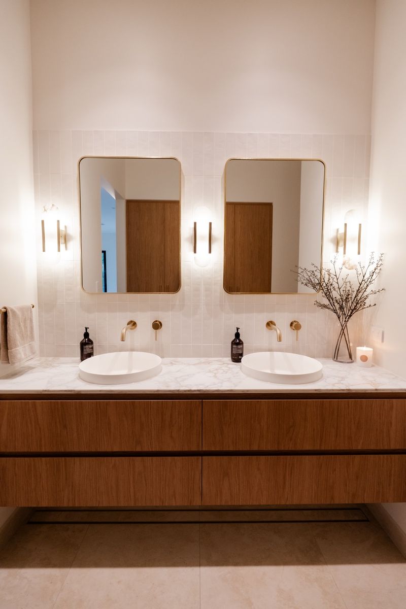 Double vanity with timber cabinetry, arched mirrors and brushed brass tapware