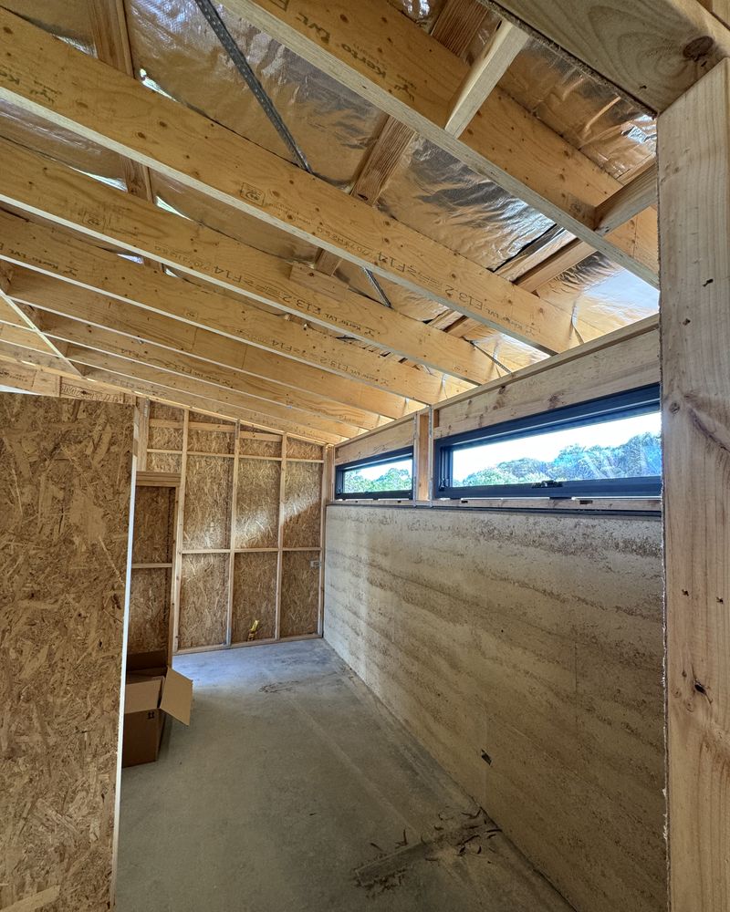 Inside the Willunga addition during framing: timber roof framing and highlight windows above a rammed-earth wall