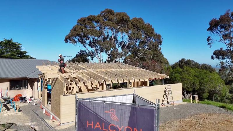 The Willunga addition under construction: curved rammed-earth walls and new roof framing beside the existing home